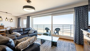 Una sala de estar moderna con un sofá de cuero, una mesa de centro de vidrio y vista al mar a través de ventanas amplias.