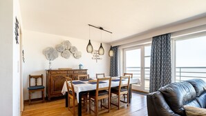Un área de comedor con una mesa y sillas de madera, un sofá de cuero oscuro, y vistas a través de un ventanal.