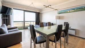 Habitación de hotel moderna con comedor, sofá, televisión de pantalla plana y ventana grande con vistas a la ciudad.