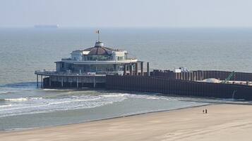 Un bâtiment situé sur la côte, surmonté d’un dôme, avec une jetée qui s’avance dans l’eau et une plage de sable.