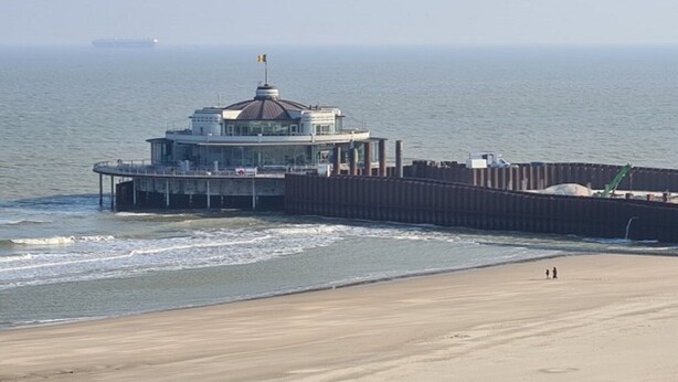 A coastal building with a dome, a pier extending into the water, and a sandy beach.
