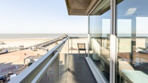 A balcony with a clear view of the beach and a chair.