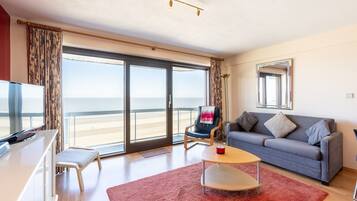A modern living room with a large sliding glass door leading to a balcony, a grey sofa, a small table, and a TV.