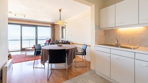 A modern kitchen with white cabinets, a marble backsplash, and a dining area with a round table and chairs. - Apartment in Blankenberge near the Pier (Blankenberge)