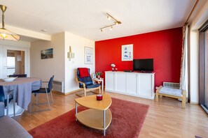 Un salon moderne avec un mur d’accent rouge, un coin repas avec une table et des chaises, un téléviseur et un petit banc.