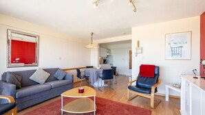A modern living room with a grey sofa, a red rug, and a dining area with a table and chairs. - Apartment in Blankenberge near the Pier (Blankenberge)