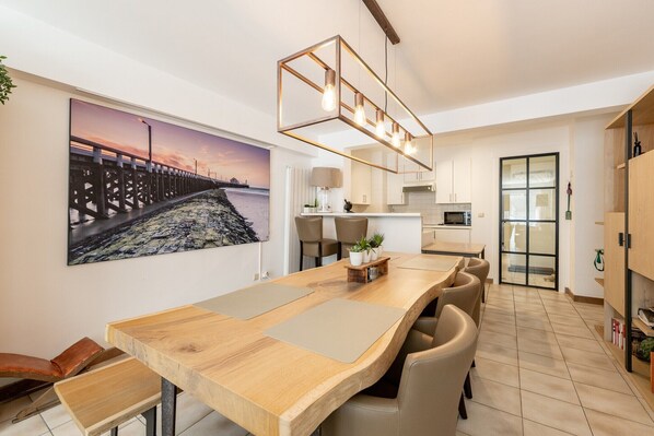 A modern kitchen with a wooden island, a dining area with chairs, and a large painting of a pier.