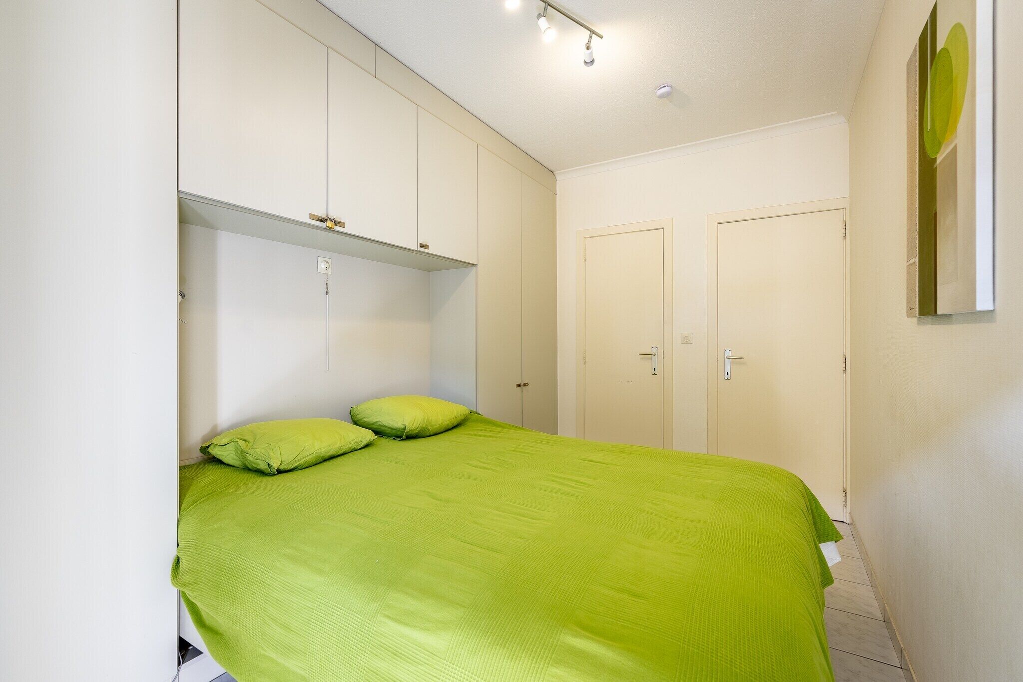 A bedroom with a bed, green bedding, and white walls.