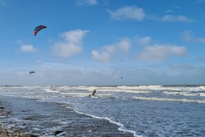 Ein Strand mit Wellen und einer Person, die Kitesurfen geht.