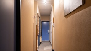 Un couloir étroit aux murs de couleur beige, une porte bleue au fond et un luminaire au plafond.