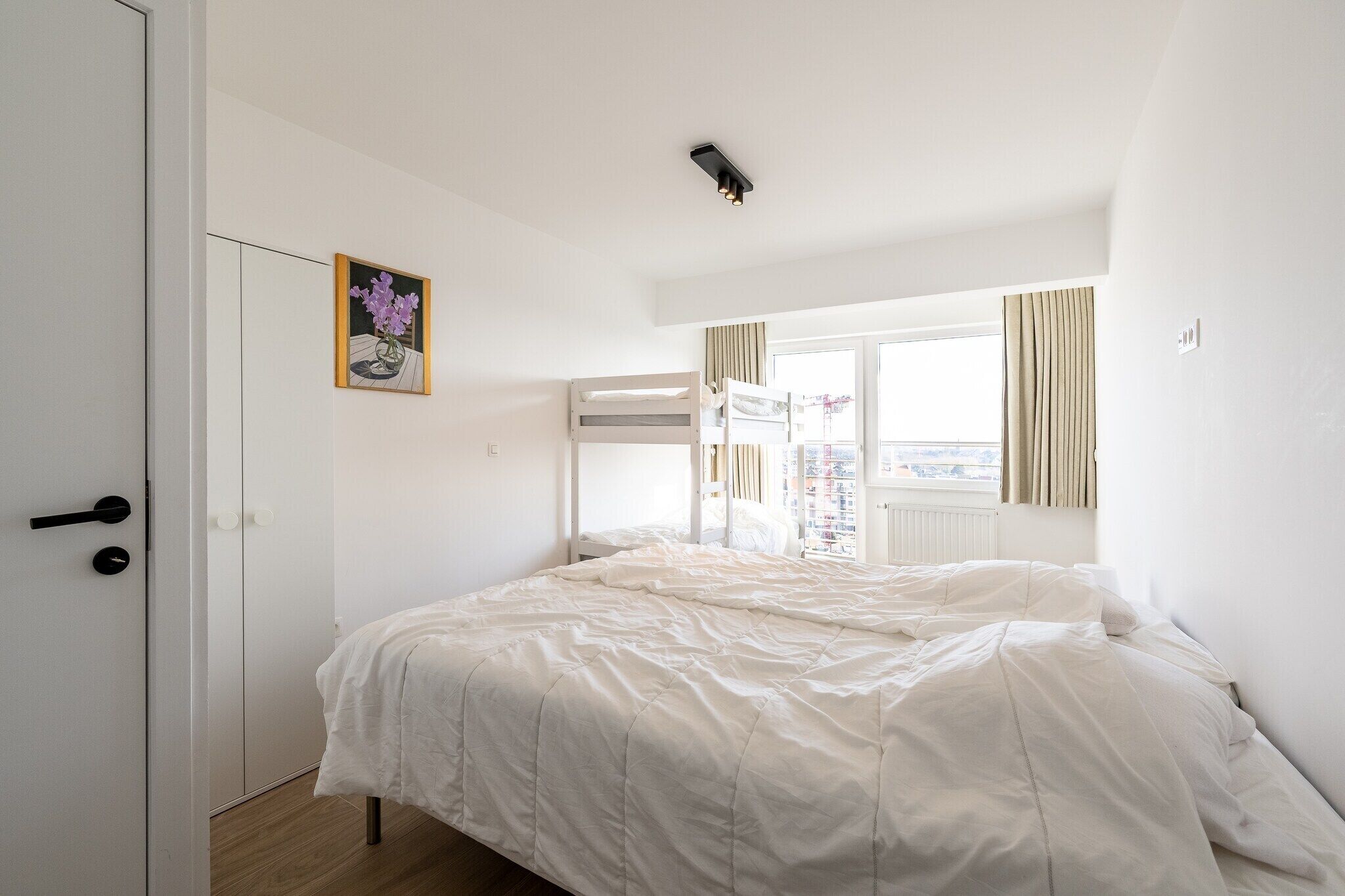 Une chambre à coucher avec un lit, une porte, une fenêtre avec des rideaux et un tableau au mur.