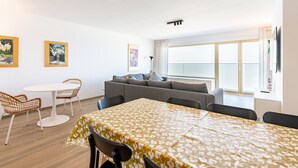 Ett modernt vardagsrum med en soffa, ett matbord med stolar och ett stort fönster med gardiner.