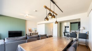 A modern living room with a large wooden dining table, grey sofas, and a TV. - Apartment in Blankenberge with Sea View (Blankenberge)