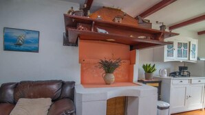 Un salon avec un canapé en cuir marron, une cheminée blanche et un coin cuisine équipé de placards et d’une machine à café.