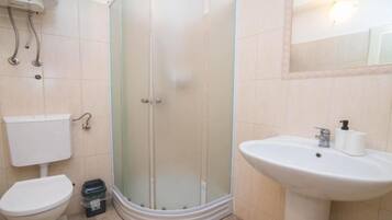 Baño con cabina de ducha de vidrio, inodoro, lavabo y espejo.