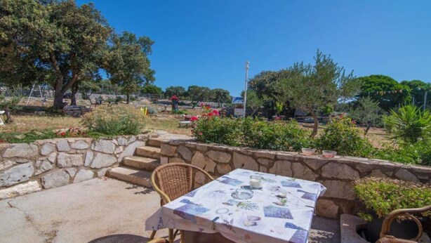 Une terrasse extérieure avec des murs en pierre, des meubles en osier et une table dressée pour le repas.