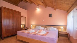 Une chambre avec une armoire en bois, un lit avec une literie rose, deux tables de chevet avec des lampes et un plafond en bois.