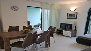 Ein modernes Wohnzimmer mit einem Holzespeisetisch, braunen Stühlen, einem Flachbildfernseher, einer Couch und einem großen Fenster mit Vorhängen.