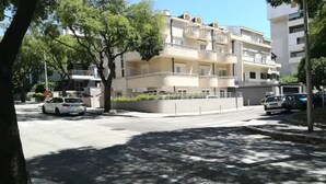 A multi-story residential building with balconies, a paved road, and parked cars.