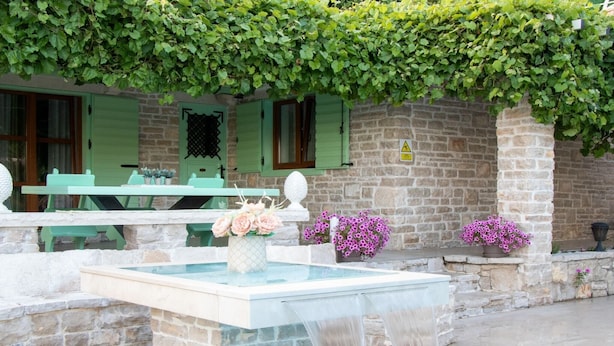 Ein Gebäude aus Stein mit Pool, grünen Fensterläden und Blumentöpfen.