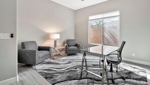 A modern living room with a glass coffee table, two armchairs, a floor lamp, and a large window with a view of a brick wall. - EAZY AZ Modern 2 bedroom townhouse on the 8th fairway of Estrella Mountain Ranch (Goodyear)