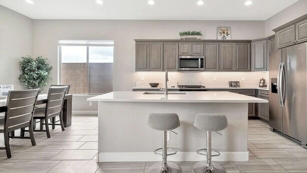 A modern kitchen with a central island, stainless steel appliances, and a dining area with a large window. - EAZY AZ Modern 2 bedroom townhouse on the 8th fairway of Estrella Mountain Ranch (Goodyear)