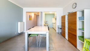 A modern kitchen with a white table, wooden cabinets, and a clock on the wall. - Apartment in Blankenberge with Sea Views (Blankenberge)