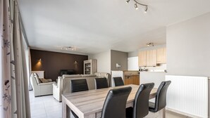 Ein modernes Wohnzimmer mit einer Couch, einem Esstisch mit Stühlen und einer Küchenzeile mit Schränken und einer Arbeitsplatte.