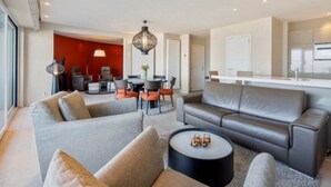 A modern living room with a grey sofa, a round coffee table, and a dining area with a table and chairs. - Apartment in Blankenberge with Ocean Views (Blankenberge)