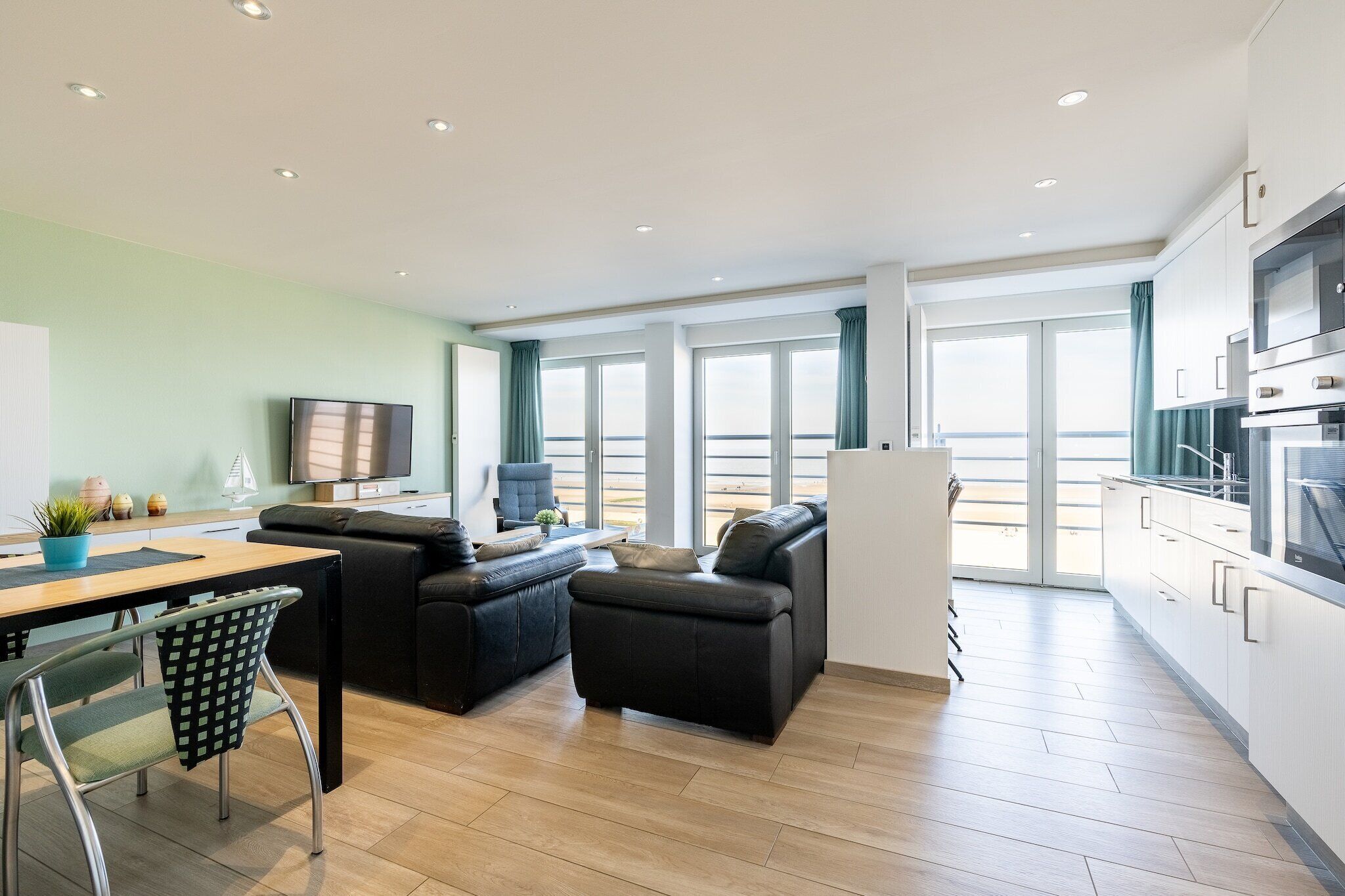 Una sala de estar moderna con un sofá, una mesa de comedor con sillas, un televisor y un balcón con vistas.