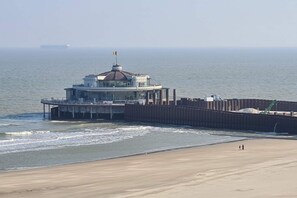 Un edificio costiero con una cupola, un molo che si protende sull'acqua e una spiaggia sabbiosa.