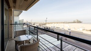 A balcony with wicker furniture overlooking a beach and pier. - Apartment in Zeedijk with Stunning Sea Views (Blankenberge)