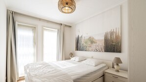 A bedroom with a large bed, a nightstand with a lamp, and a painting on the wall. - Apartment in Zeedijk with Stunning Sea Views (Blankenberge)