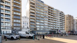 A multi-story residential building with balconies, a pedestrian area with benches, and a small kiosk. - Apartment in Zeedijk with Stunning Sea Views (Blankenberge)