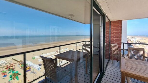 A balcony with a view of the beach, wooden furniture, and a glass door leading to the interior. - Apartment by North Sea with Ocean Views (Blankenberge)