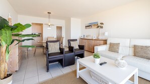 A modern living room with a white sofa, two black armchairs, a white coffee table, and a dining area with a wooden cabinet and chairs. - Apartment in Blankenberge with Sea Views (Blankenberge)