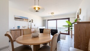 A dining area with a round wooden table, cushioned chairs, and pendant lighting. - Apartment in Blankenberge with Sea Views (Blankenberge)