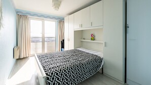 Quarto com cama, guarda-roupa, prateleira pequena com objetos decorativos e porta de vidro deslizante que dá para uma varanda.