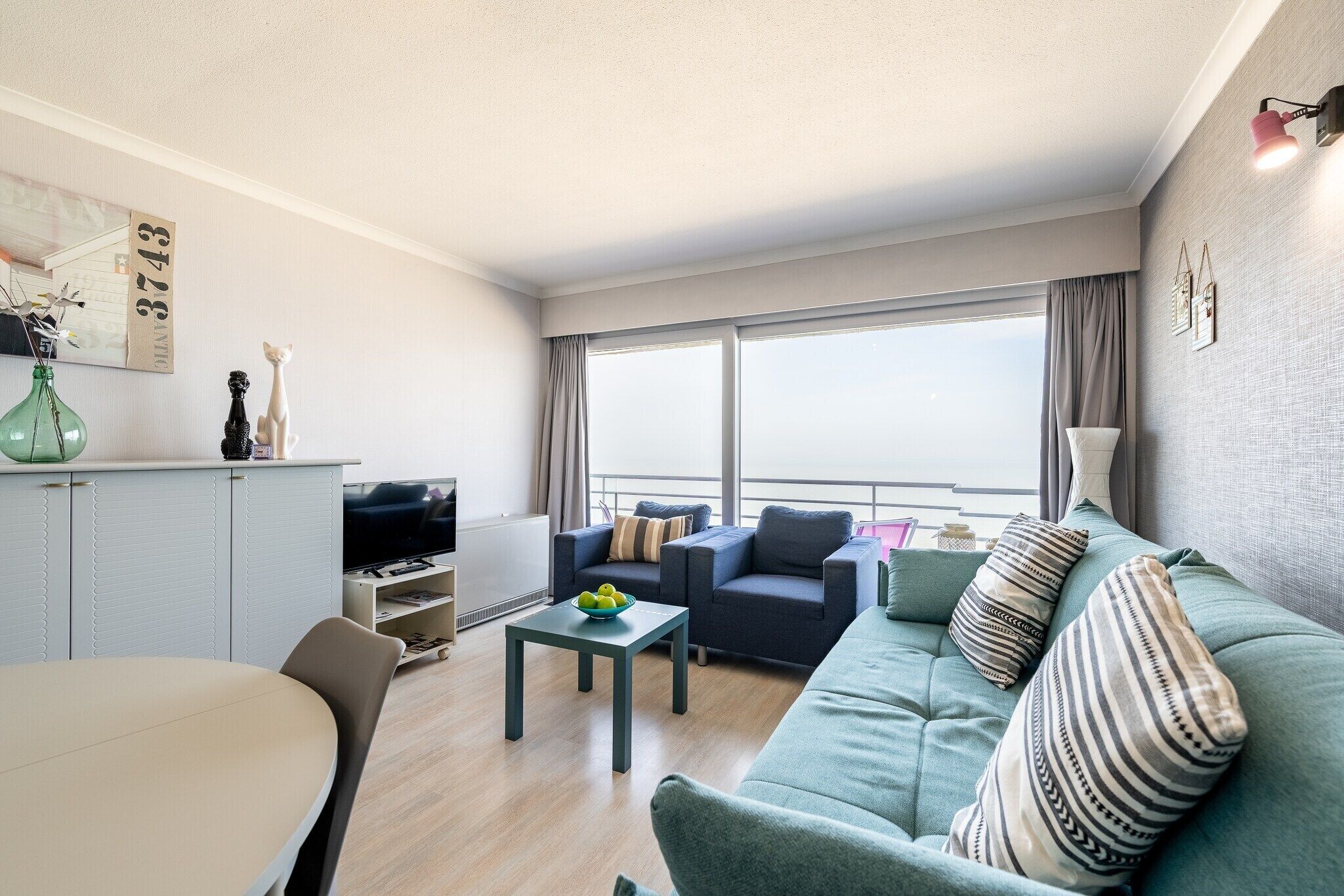 Een moderne woonkamer met een bank, een salontafel en een televisie. Er is een raam met gordijnen en uitzicht op het buiten.