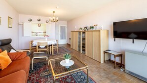 Ein Wohnzimmer mit Sofa, Couchtisch, Fernseher, Essbereich mit Tisch und Stühlen sowie einer Vitrine.