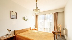 A hotel room with a large bed, a wooden nightstand, a desk lamp, a chair, a hanging plant, and a chandelier. - Apartment in Blankenberge near Belgian Pier (Blankenberge)