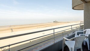 A balcony with a view of a beach and a pier. There are white plastic chairs and a railing. - Apartment in Blankenberge near Belgian Pier (Blankenberge)