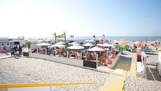 Ein Restaurant direkt am Strand mit Außenbereich, Sonnenschirmen, einem Sandstrand und freiem Blick auf das Meer.
