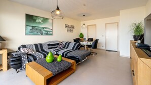 Ein modernes Wohnzimmer mit einer Couch, einem Couchtisch und Pendelleuchten. Es gibt eine Essecke mit Tisch und Stühlen.
