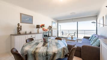 A dining area with a table set for two, a sofa, and a balcony with a view.