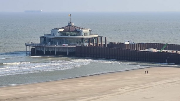 Ein Küstengebäude mit Kuppel, einem Steg, der ins Wasser führt, und einem Sandstrand.