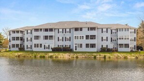 A multi-story apartment building with a flat roof, large windows, and a grassy area in front. - Sanibel Summer Hideaway | Waterfront Oasis (Rehoboth Beach)