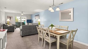 A modern living room with a dining area, grey sofas, a wooden dining table, and light blue walls. - Sanibel Summer Hideaway | Waterfront Oasis (Rehoboth Beach)