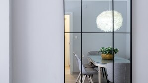 Un comedor con una mesa de vidrio, sillas grises tapizadas y una lámpara esférica blanca colgante.