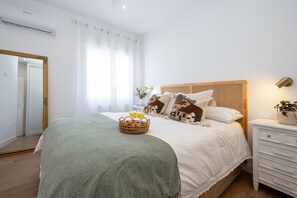 A neatly arranged bedroom with a bed, bedside table, and a basket of bread and juice.